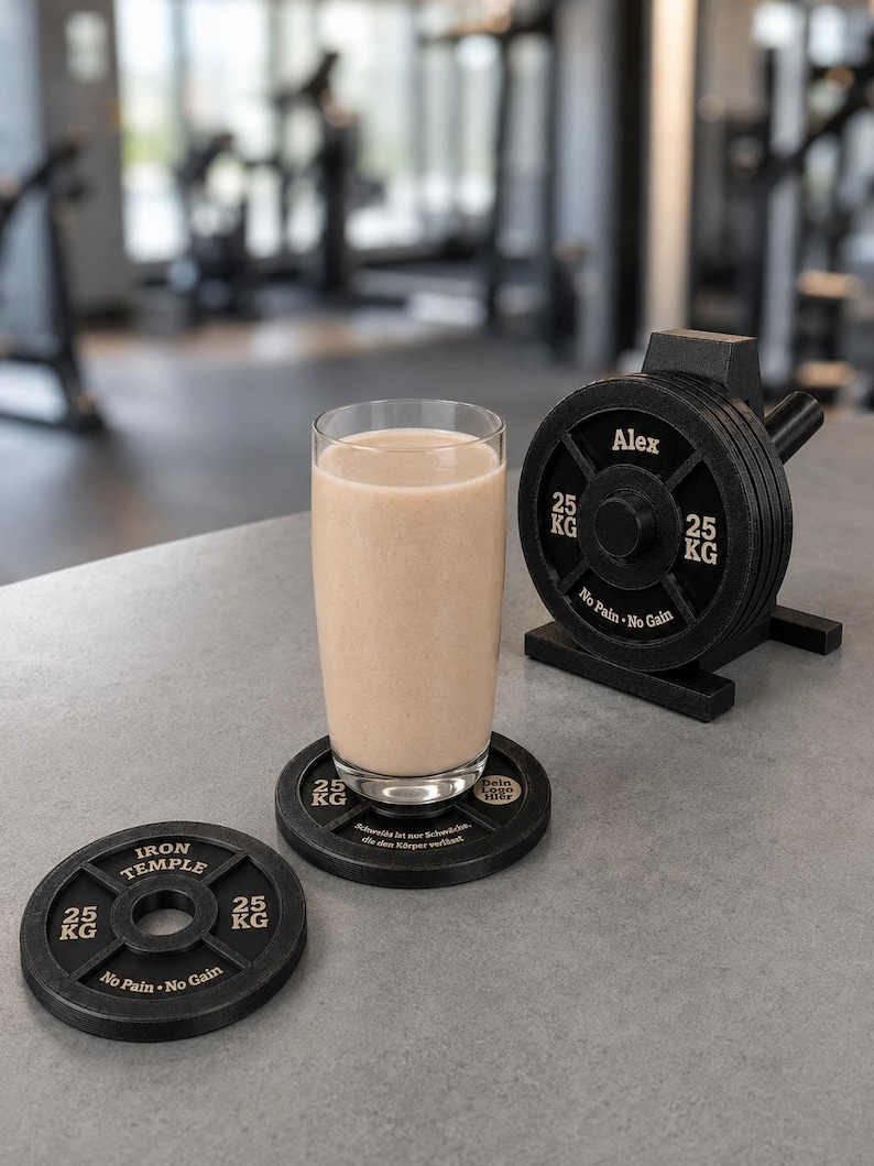 May include: A clear glass filled with a beige protein shake sits on a black coaster shaped like a 25 kg weight plate. Another matching coaster lies nearby, and a small black weight plate rack holds several plates labeled Alex and No Pain No Gain.