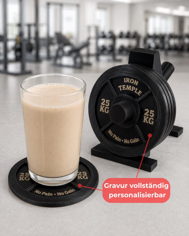 May include: A clear glass filled with a beige protein shake resting on a black circular coaster shaped like a weight plate. Next to it is a black weight plate stand with the text IRON TEMPLE, 25 KG, and No Pain No Gain engraved on it.