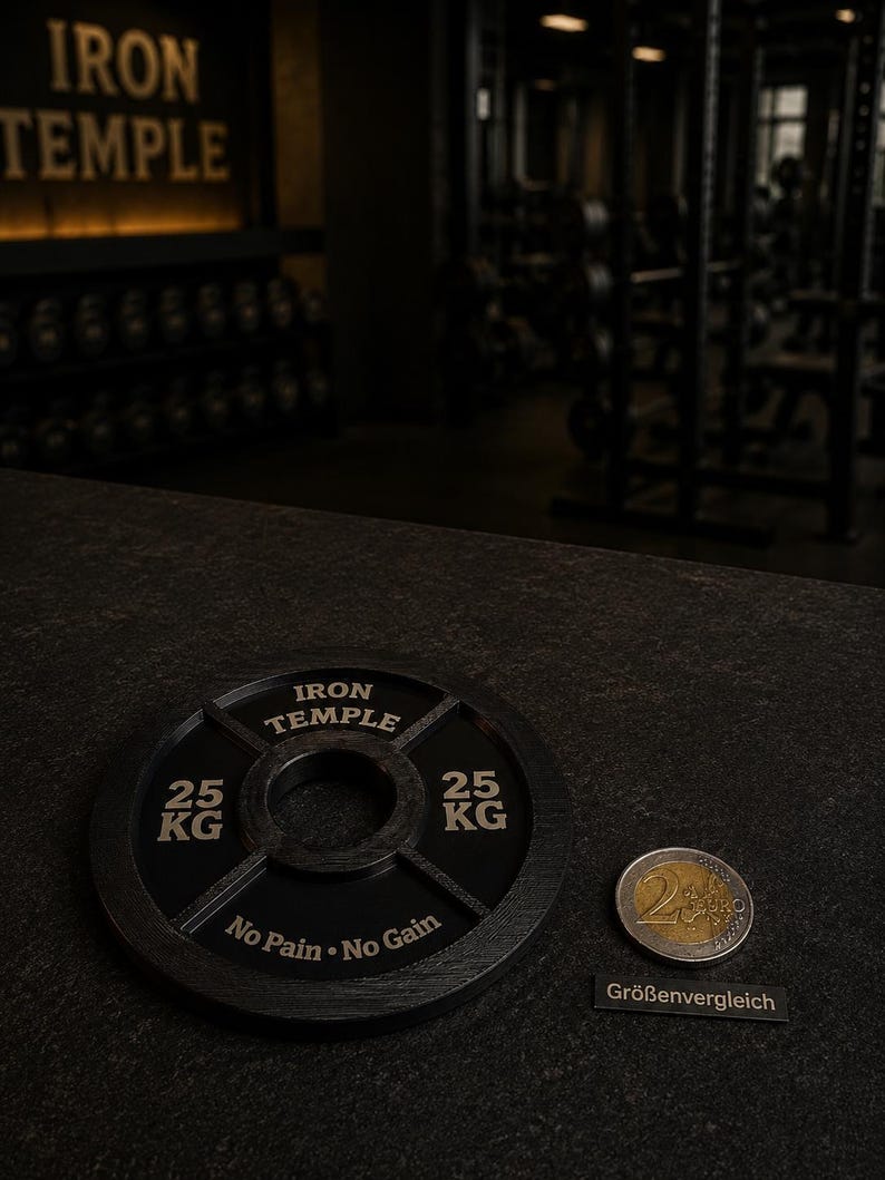 May include: A black circular weight plate featuring the text IRON TEMPLE, 25 KG, and No Pain No Gain, positioned next to a two-euro coin for scale. The weight plate has a central hole and structural spokes, with a dark, textured finish throughout.