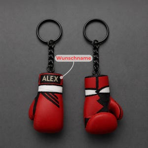 May include: Two red and black boxing glove keychains with black metal rings and chains. The left glove features the name ALEX in white text on a black rectangular patch, with a white band above it. A line points to the name with the text Wunschname.