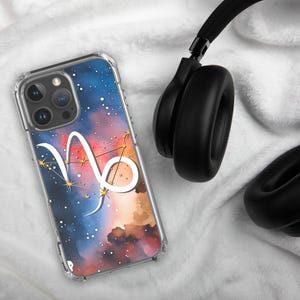 Könnte beinhalten: Transparente Handyhülle mit einem Capricorn-Sternzeichen-Design. Die Hülle hat einen Aquarellhintergrund in Blau, Rot und Braun, mit weißen Sternen und einer Konstellation. Schwarze Kopfhörer befinden sich im Hintergrund.