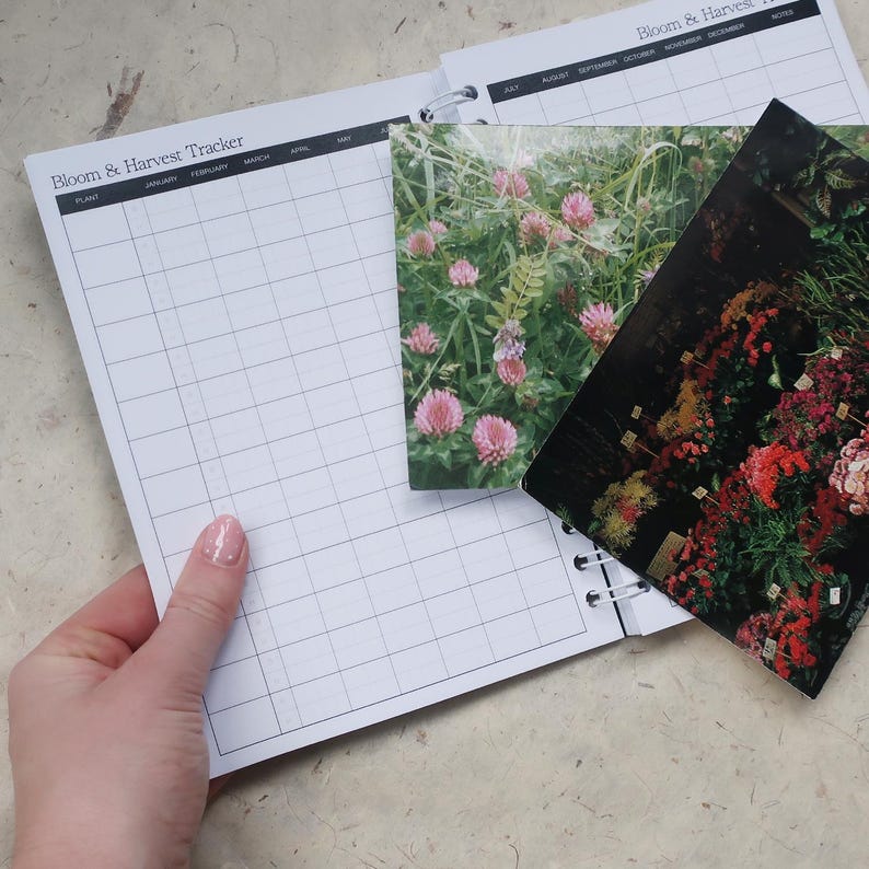 May include: A spiral-bound Bloom & Harvest Tracker planner with a grid layout for tracking plants from January to December. Two rectangular photo inserts are placed on the pages, one showing pink clover flowers and the other a garden display.