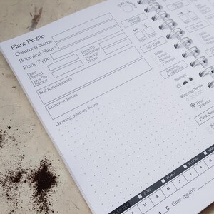 May include: A white spiral-bound garden planner page featuring a Plant Profile section with fields for common name, botanical name, plant type, dates, soil requirements, and growing journey notes, plus icons for sunlight, watering, and frost tolerance.