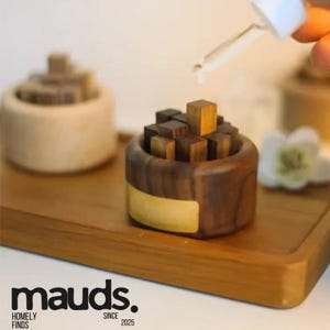 Puede incluir: Un difusor de aceites esenciales de madera con acabado marrón oscuro y marrón claro. El difusor está lleno de pequeños bloques de madera. Se sostiene un cuentagotas sobre el difusor. El difusor se encuentra sobre una bandeja de madera.