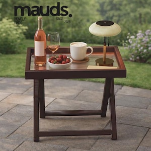 May include: A dark brown wooden serving table with a tray top, holding a bottle of rosé wine, a wine glass, a bowl of strawberries, and a white mug. A small lamp sits on the tray. The text "mauds. HOMELY FINDS SINCE 2025" is at the top.