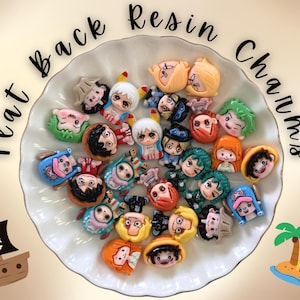 May include: A collection of small, colorful flat back resin charms featuring various cartoon character faces with diverse hair colors and expressions, arranged in a white scalloped bowl. The text "Flat Back Resin Charms" is arched above.