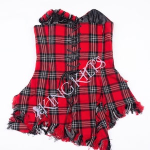 May include: A strapless corset top featuring a red, black, and white tartan pattern. The garment includes a black lace-up front closure with black cord, a black interior lining, and a frayed, uneven hemline. The text KING KILTS is visible.
