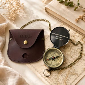 May include: A brass pocket compass with a chain and a dark brown leather pouch. The compass lid is engraved with the text: For all the adventures to come. Love, Dad. The leather pouch features the embossed initials O.B.L. and a gold-tone snap.