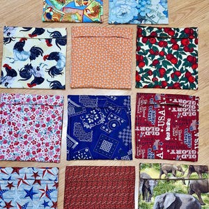May include: A collection of ten square fabric pouches featuring diverse patterns including roosters, floral prints, red apples, blue bandanas, patriotic USA text, stars, geometric textures, and a wildlife scene with elephants in a grassy field.