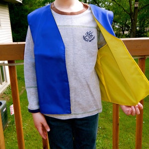 May include: A child wearing a blue and yellow safety vest with the text "Forest Patrol" on the front.