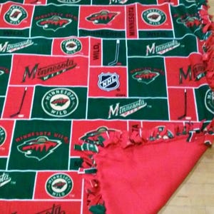 May include: A red and green fleece tie blanket with the Minnesota Wild NHL team logo. The blanket is tied in a knot pattern.