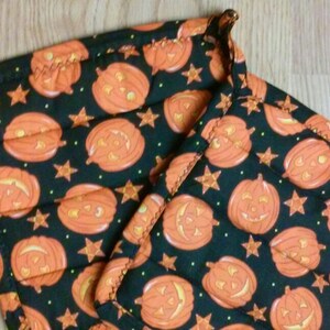 May include: Two black fabric pot holders with a Halloween theme. The pot holders are covered in a pattern of orange jack-o'-lantern faces and yellow stars on a black background.