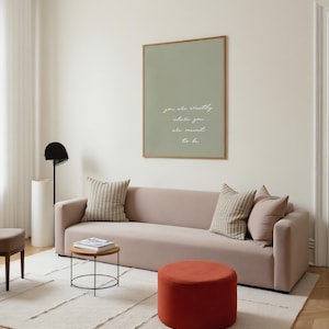 Puede incluir: Un sal&oacute;n moderno con un sof&aacute; rosa claro, cojines y una mesa auxiliar redonda. Una impresi&oacute;n enmarcada en la pared dice "you are exactly where you are meant to be". La habitaci&oacute;n incluye un puf rojo y una alfombra color crema.