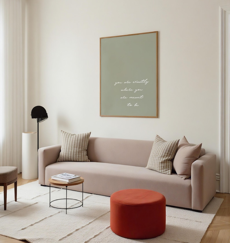 Puede incluir: Un sal&oacute;n moderno con un sof&aacute; rosa claro, cojines y una mesa auxiliar redonda. Una impresi&oacute;n enmarcada en la pared dice "you are exactly where you are meant to be". La habitaci&oacute;n incluye un puf rojo y una alfombra color crema.