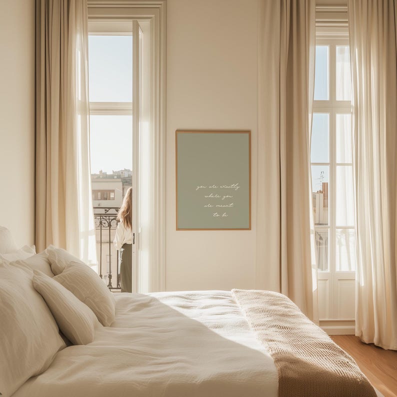 Puede incluir: Una escena de dormitorio con una cama cubierta con s&aacute;banas y almohadas blancas. Un estampado verde salvia enmarcado con texto blanco cuelga de la pared. El texto dice: "eres digno, lo que tambi&eacute;n quieras ser". Cortinas beige enmarcan ventanas abiertas.