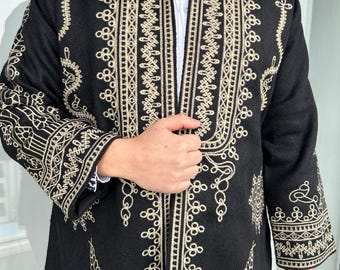 Può includere: Cappotto nero con ricami beige intricati. Il cappotto presenta motivi dettagliati lungo i bordi, le maniche e la parte anteriore, creando un contrasto sorprendente. È indossato sopra una camicia bianca con colletto.