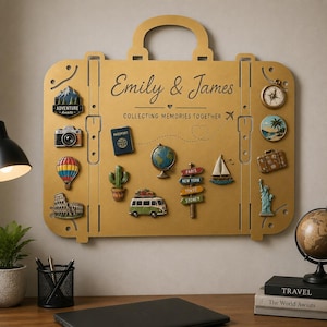 May include: A gold-colored metal wall display shaped like a suitcase, featuring the text "Emily & James" and "COLLECTING MEMORIES TOGETHER." It is decorated with various travel-themed magnets, including a camera, globe, passport, and landmarks.