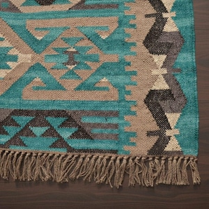 Puede incluir: Una alfombra rectangular con un patrón geométrico en verde azulado, marrón y gris. La alfombra tiene flecos en un borde. El diseño presenta formas y patrones repetidos, creando un aspecto texturizado. Adecuado para la decoración del hogar.