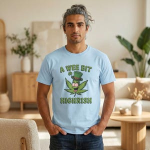 Könnte beinhalten: Hellblaues T-Shirt mit dem Text "A Wee Bit Highrish" und einer Cartoon-Cannabisblatt-Figur mit grünem Hut. Die Grafik ist in Grün und Pink gehalten. Das Shirt ist aus einem weichen Material.