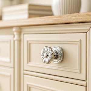 Puede incluir: Primer plano de un armario color crema con un tirador plateado en forma de flor. El mueble tiene una encimera de madera. El tirador es el punto focal, añadiendo un toque decorativo.