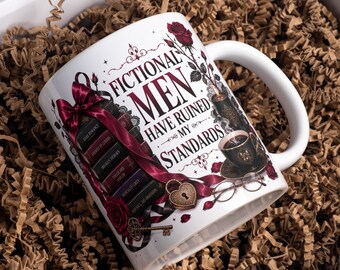 May include: A white ceramic mug featuring a stack of books with titles like Dark Romance and Morally Grey, a burgundy ribbon, a heart-shaped padlock, a key, a cup of coffee, and red roses. The text reads, FICTIONAL MEN HAVE RUINED MY STANDARDS.