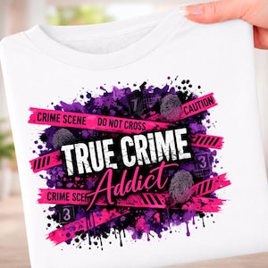 May include: A white t-shirt featuring a graphic design with purple paint splatters, pink crime scene tape with the text "CRIME SCENE DO NOT CROSS" and "CAUTION", fingerprint icons, and the bold white and pink text "TRUE CRIME Addict".