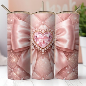 May include: A set of three pink tumblers with a bow and heart design. The tumblers feature a quilted pattern, a large satin bow, and a heart-shaped jewel. Each tumbler has a gold-colored straw.