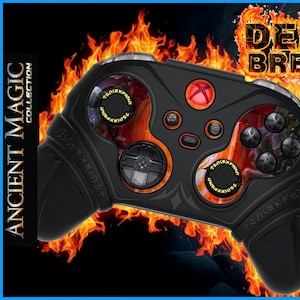 Peut inclure: Manette de jeu noire avec des accents orange et rouges, avec le texte "DEMON BREAKER" dans une police enflammée. La manette a un design avec les mots "ANCIENT MAGIC COLLECTION" sur le côté. Un guerrier se tient en arrière-plan.