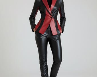 Op de afbeelding: Een zwart en rood leren pak. De blazer heeft een rode revers en rode verticale strepen. De broek is van zwart leer. Het model draagt een zwarte coltrui en zwarte laarzen. Het pak is een strak, modern ontwerp.