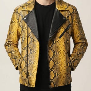 May include: A yellow and black snakeskin-patterned leather jacket with a black collar and zip closure. The jacket has a classic biker style with a notched lapel and a fitted silhouette. The model is wearing a black shirt underneath.