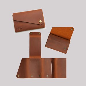 May include: A collection of brown leather wallets in various stages of opening and closing. One wallet is closed with the initials "MKC" embossed on the front. The wallets feature snap closures and a natural leather interior.