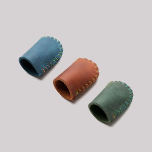 May include: Three leather finger protectors in blue, brown, and green. Each has a scalloped edge with contrasting yellow and orange stitching. The finger sleeves are designed to protect the fingers.