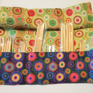 Puede incluir: Un estuche enrollable de tela con un patrón circular colorido en tonos de verde, rojo, marrón y blanco. El estuche está lleno de agujas de tejer de madera de varios tamaños.