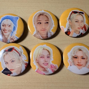 May include: A set of six circular pin-back buttons featuring individual photographic portraits of a person with blonde hair against a solid yellow background. Each button displays a different facial expression, including smiling, winking, and posing with hands near the face, with some portraits showing red-rimmed sunglasses.