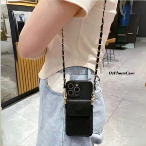 May include: Black quilted leather phone case with a gold chain strap. The case has a small pocket on the front and a gold clasp. The phone case is designed to be worn around the neck or across the body.