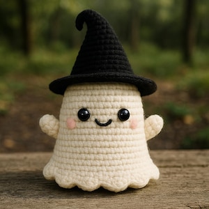 Puede incluir: Muñeca fantasma de ganchillo con un sombrero de bruja negro. El fantasma es de color crema con mejillas rosadas, ojos negros y una boca sonriente. La muñeca tiene brazos pequeños y un borde inferior festoneado. El fondo es una escena borrosa del bosque.