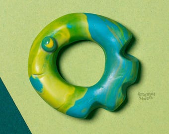 May include: A colorful, fish-shaped toy with a hole in the center, in shades of yellow, green, and blue. The toy is set against a two-tone background of green and teal. The text "underwater silence" is at the top.