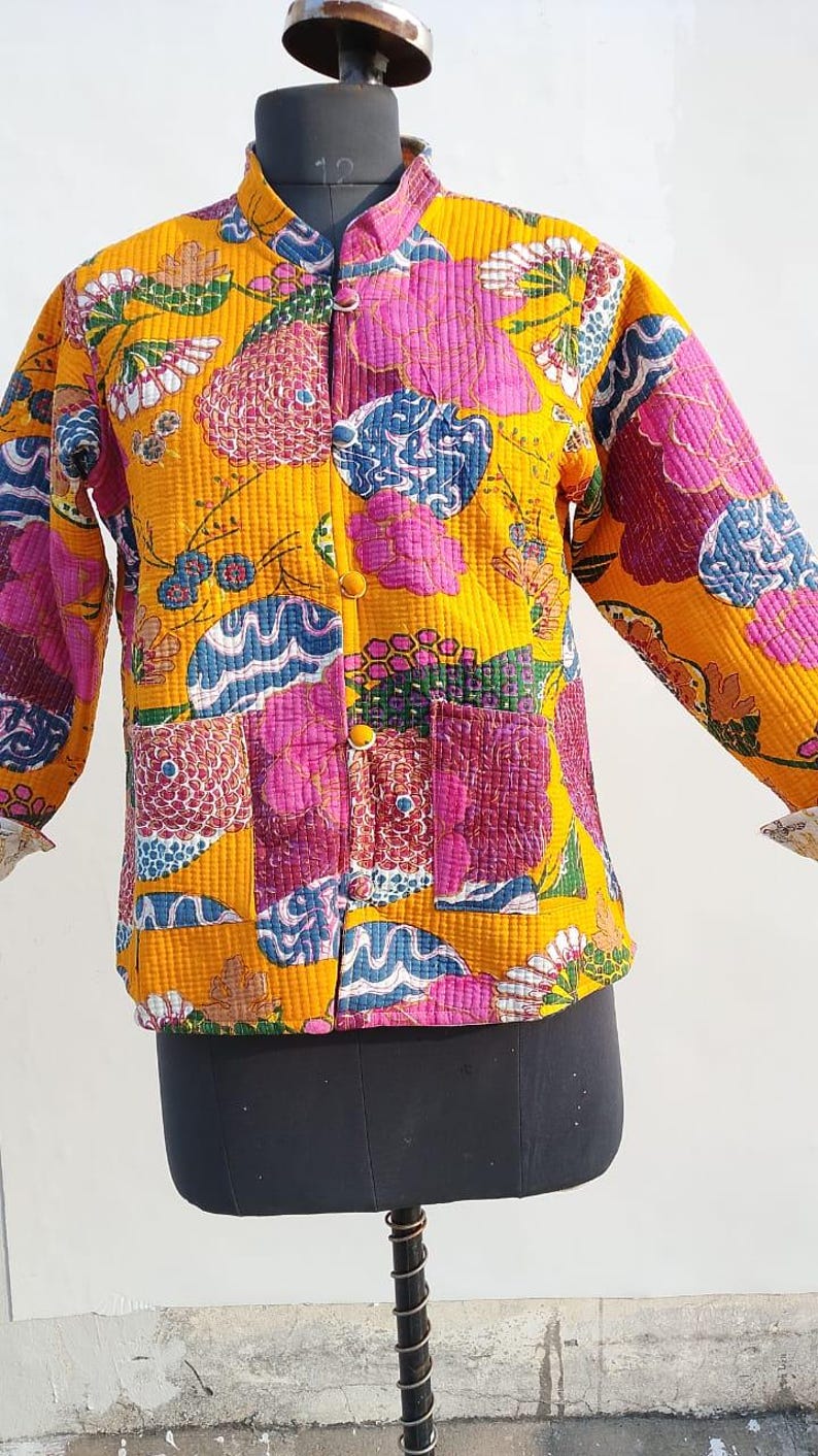 May include: A quilted jacket featuring a vibrant mustard yellow base with a multi-colored floral and abstract pattern in shades of pink, blue, and green. The jacket has a mandarin collar, long sleeves, a front button closure, and two pockets.