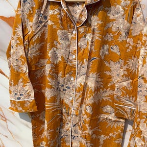 Pode incluir: Conjunto de pijama mostarda com um padr&atilde;o floral em creme e azul marinho. O conjunto inclui uma camisa com bot&otilde;es com debrum branco e cal&ccedil;as a condizer. O tecido parece leve e confort&aacute;vel.