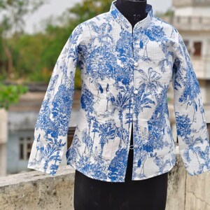 May include: A white and blue quilted jacket with a stand-up collar and long sleeves. The jacket features a blue botanical print with trees and birds. It is buttoned up the front and displayed on a black mannequin.