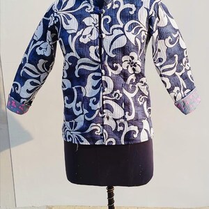 May include: A long-sleeved quilted jacket featuring a dark blue and white floral pattern. The jacket has a mandarin collar, a front button closure with fabric-covered buttons, and cuffs that reveal a contrasting pink and blue patterned lining.