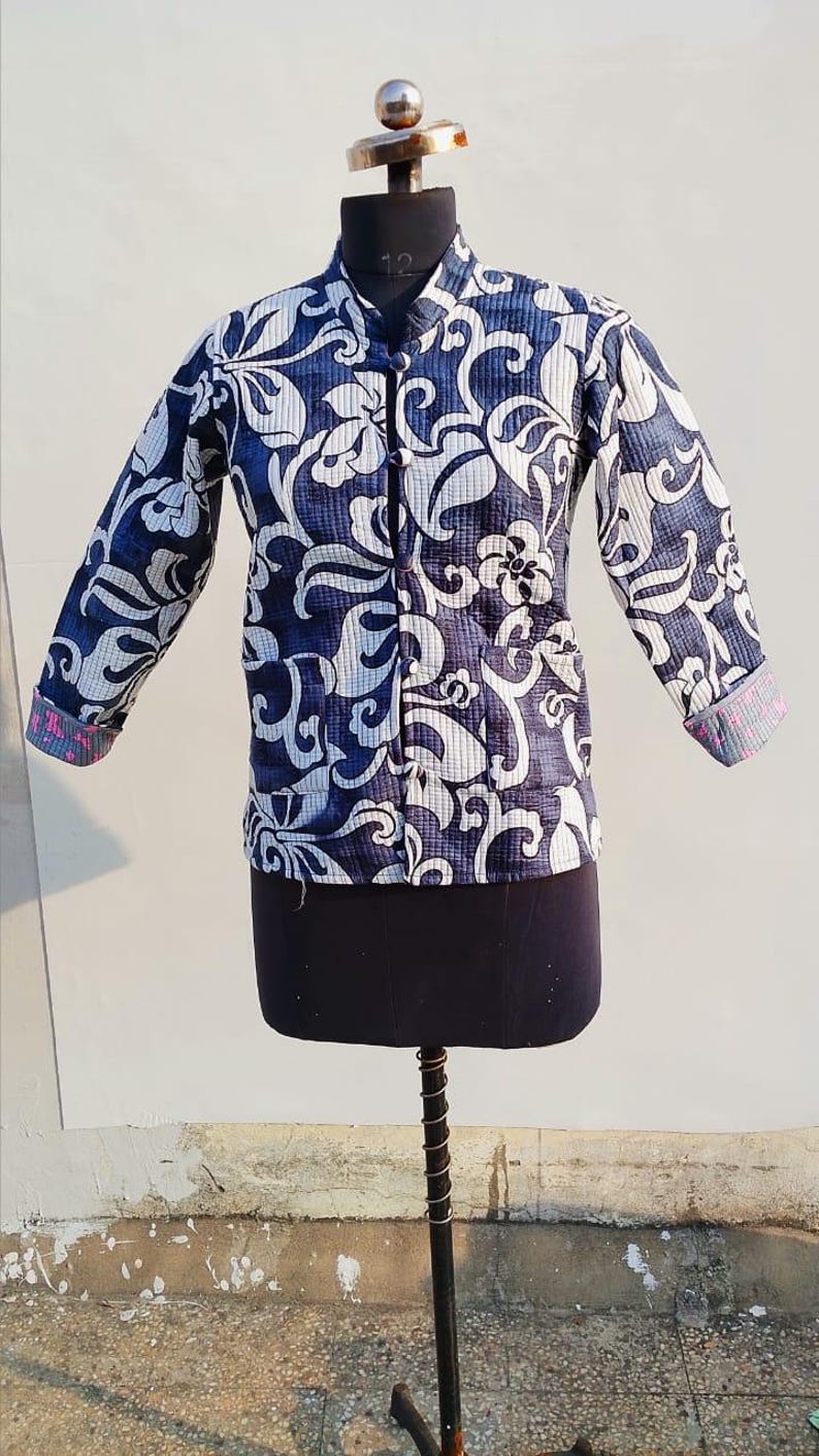 May include: A long-sleeved quilted jacket featuring a dark blue and white floral pattern. The jacket has a mandarin collar, a front button closure with fabric-covered buttons, and cuffs that reveal a contrasting pink and blue patterned lining.