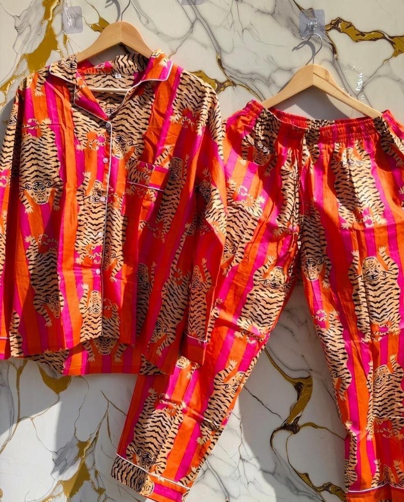 K&ouml;nnte beinhalten: Ein lebendiges Pyjama-Set mit Tigerstreifenmuster in Orange, Pink und Schwarz. Das Set beinhaltet ein Hemd mit Kn&ouml;pfen und Brusttasche sowie eine passende Hose. Wei&szlig;e Paspeln akzentuieren Kragen, Manschetten und Tasche.