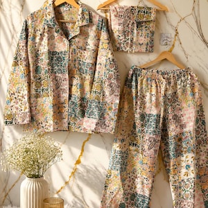 May include: A long-sleeved button-down shirt and matching wide-leg trousers featuring a multi-colored floral and paisley patchwork print in shades of yellow, blue, green, and pink, displayed on wooden hangers with a small folded fabric square.