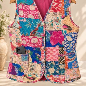 Könnte beinhalten: Eine ärmellose, gesteppte Weste mit einem lebendigen Patchwork-Design aus Blumen- und geometrischen Mustern in Rosa-, Blau- und Orangetönen. Die Weste hat einen V-Ausschnitt, vier stoffbezogene Knöpfe, zwei Vordertaschen und ein XL-Größenetikett.