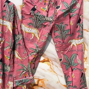 Może przedstawiać: R&oacute;żowy zestaw piżamowy z tropikalnym nadrukiem przedstawiającym zebry, lamparty, tukany i palmy. Zestaw zawiera top z długim rękawem i spodnie ze sznurkiem w pasie i białym wykończeniem.