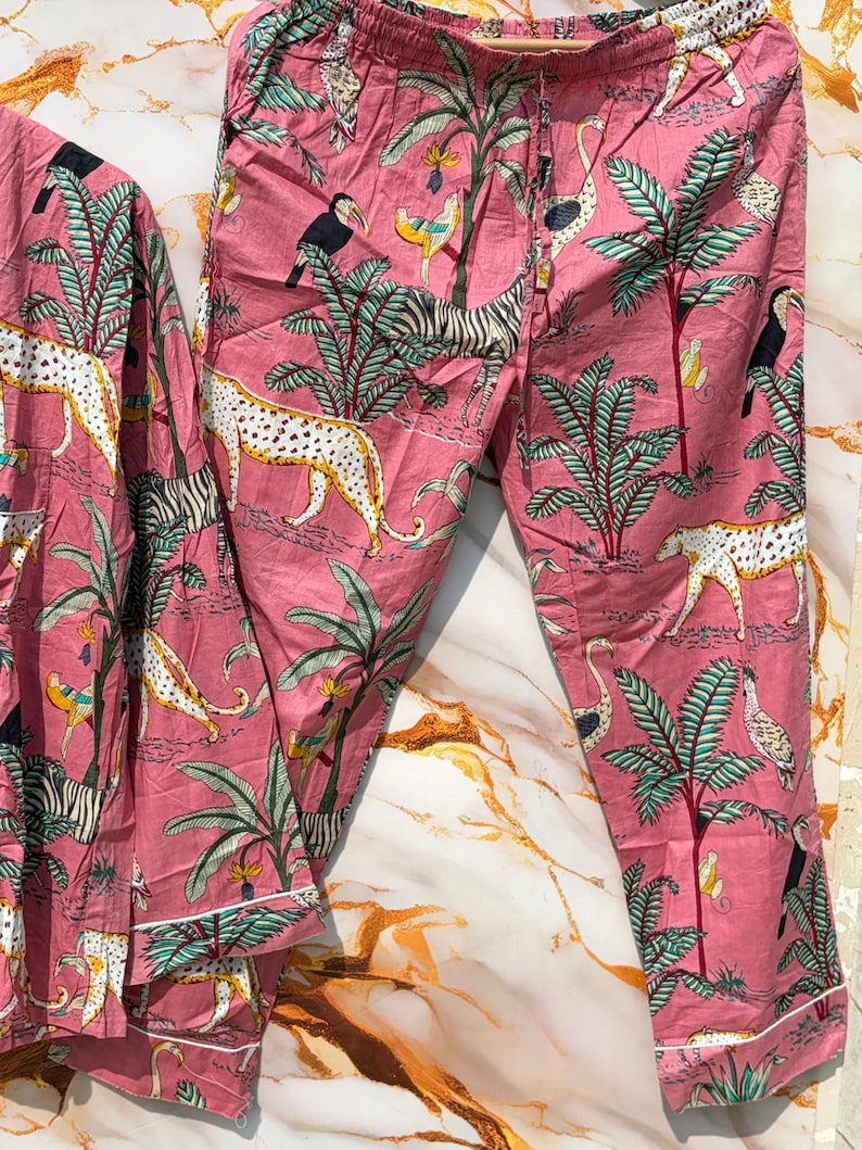 Może przedstawiać: R&oacute;żowy zestaw piżamowy z tropikalnym nadrukiem przedstawiającym zebry, lamparty, tukany i palmy. Zestaw zawiera top z długim rękawem i spodnie ze sznurkiem w pasie i białym wykończeniem.