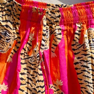 K&ouml;nnte beinhalten: Nahaufnahme einer bunten Hose mit Tigerstreifenmuster. Die Hose hat einen Kordelzug in der Taille und ist aus leichtem Stoff gefertigt. Das Farbschema umfasst Orange, Pink und Schwarz.