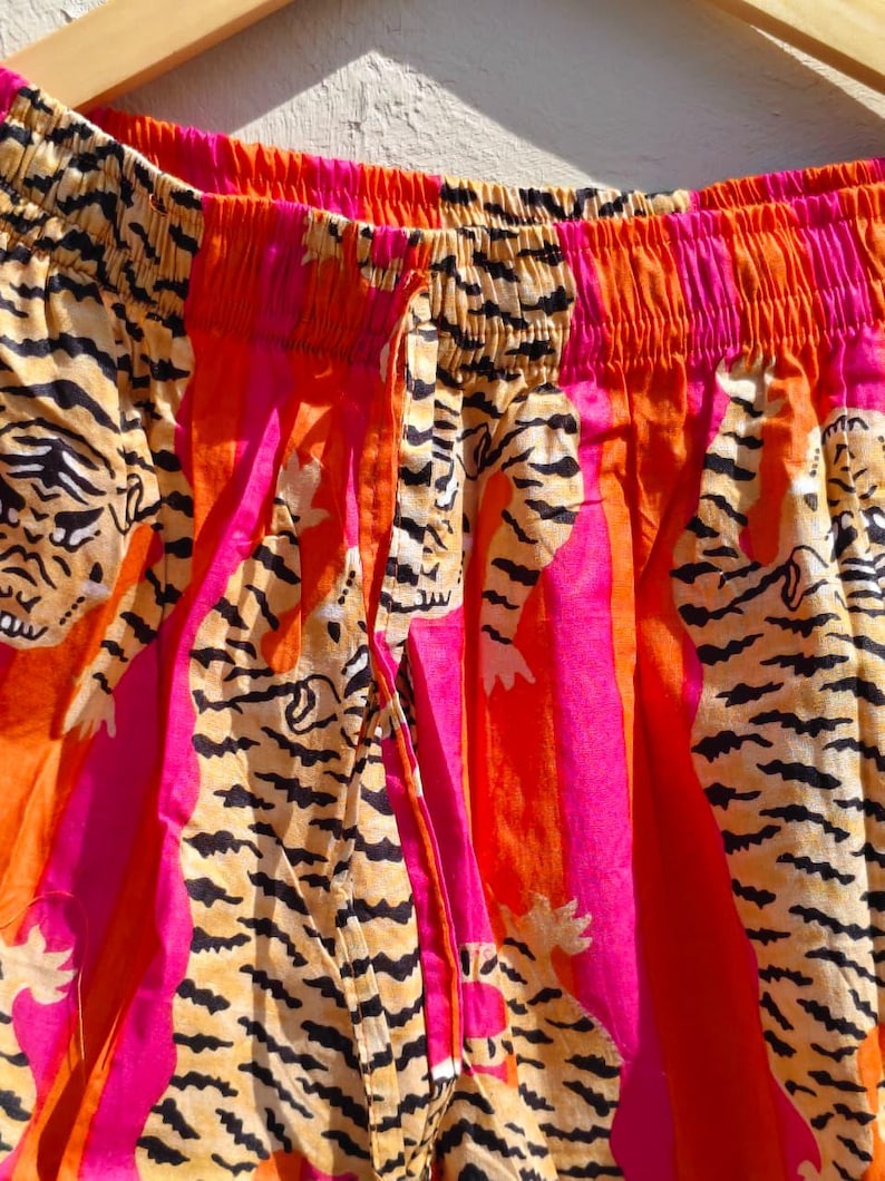 K&ouml;nnte beinhalten: Nahaufnahme einer bunten Hose mit Tigerstreifenmuster. Die Hose hat einen Kordelzug in der Taille und ist aus leichtem Stoff gefertigt. Das Farbschema umfasst Orange, Pink und Schwarz.