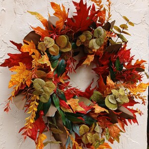 Couronne d'automne colorée. Décoration de porte automnale avec des feuilles rouges, jaunes, oranges et vertes. Couronne cadeau pour une pendaison de crémaillère.